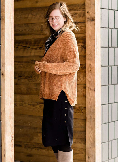 Woman wearing an open front cardigan that is chenille and camel in color. She is also wearing it over a black dress and brown riding boots. She is standing on the stairs at Inherit Clothing Company.