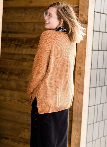 Woman wearing an open front cardigan that is chenille and camel in color. She is also wearing it over a black dress and brown riding boots. She is standing on the stairs at Inherit Clothing Company.