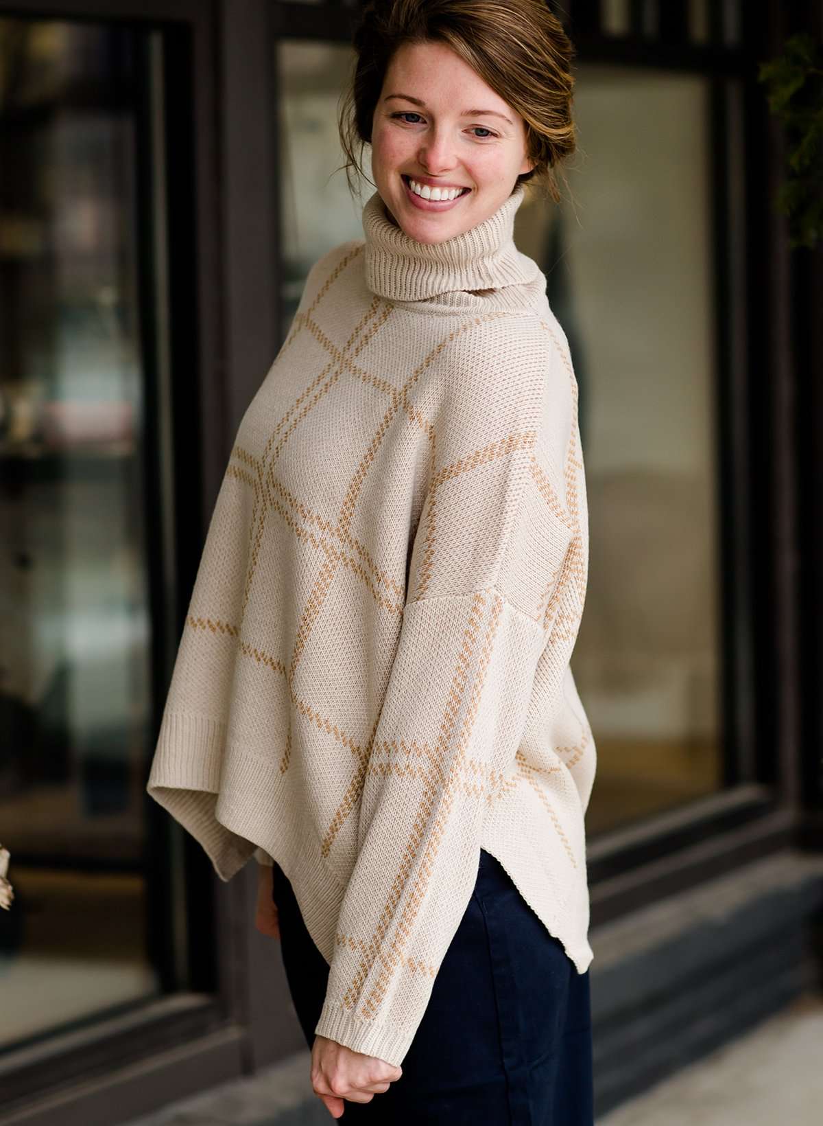 Woman wearing a shawl like sweater that is cream with a gold and orange subtle design.