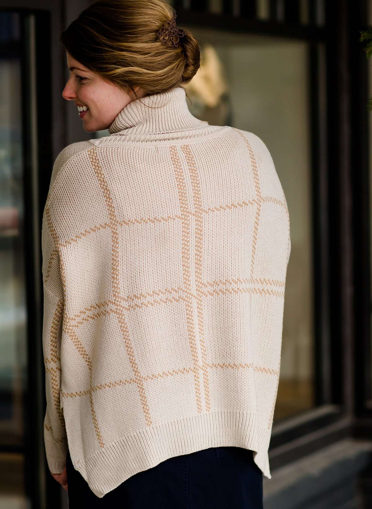 Woman wearing a shawl like sweater that is cream with a gold and orange subtle design.