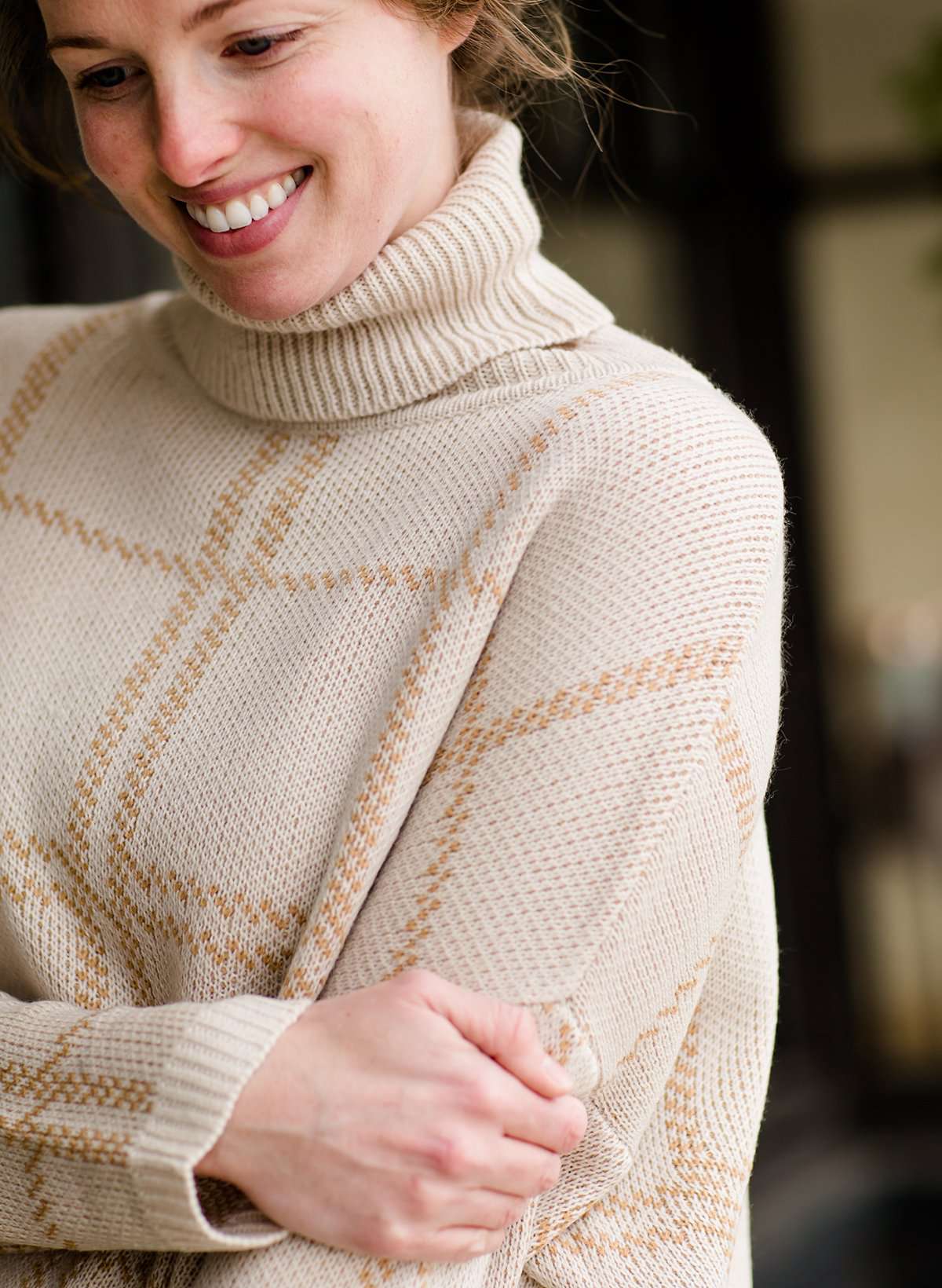 Woman wearing a shawl like sweater that is cream with a gold and orange subtle design.