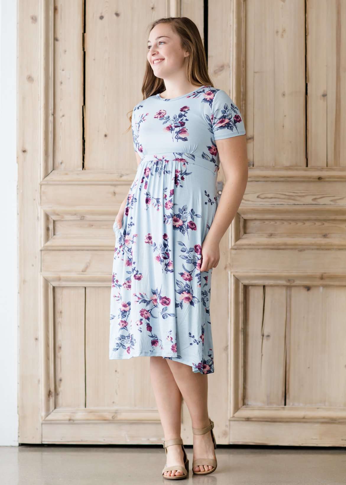 Woman wearing a light blue modest empire waist midi dress with flowers on it