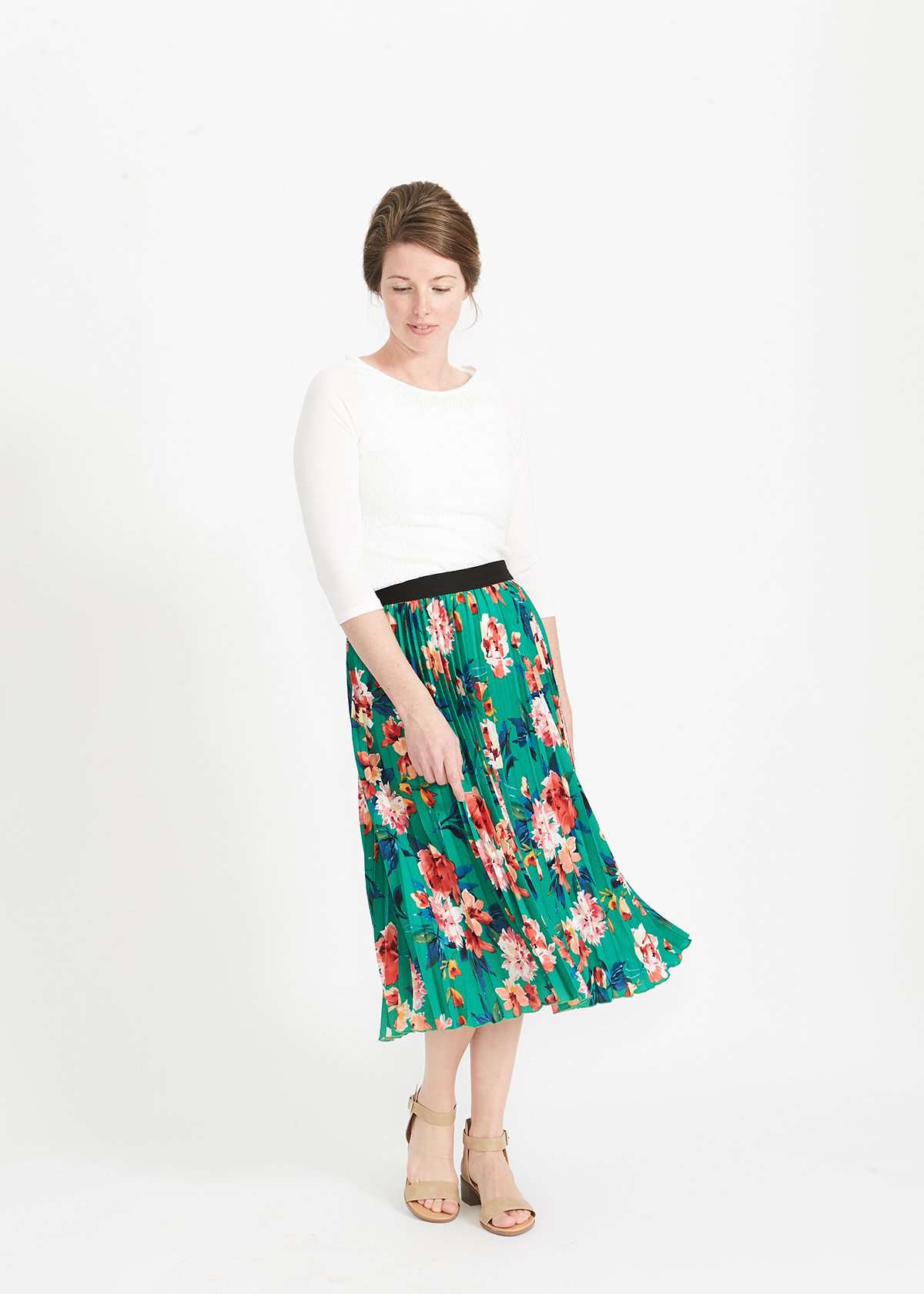 Woman wearing an emerald green floral stretchy pleated swing skirt with dress shoes and a white lace top